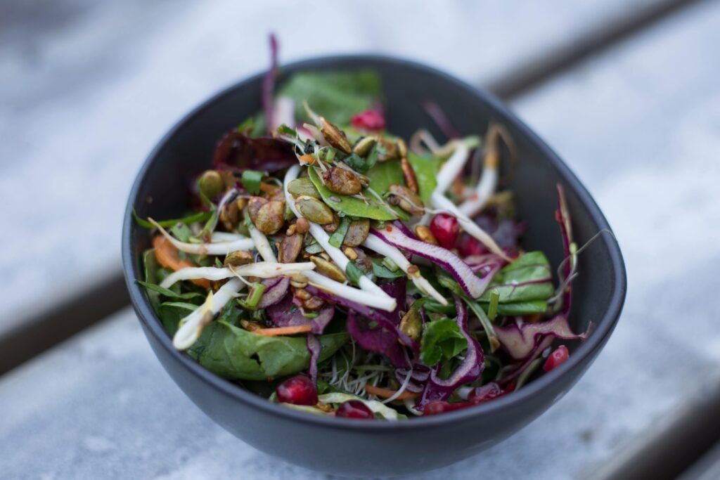 Vibrant salad with mixed greens, nuts, and pomegranate in a black bowl.